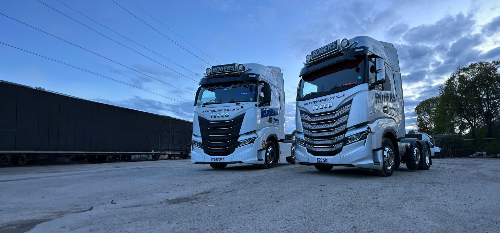 Two white Rogers Transport IVECO lorries parked at the yard at dusk