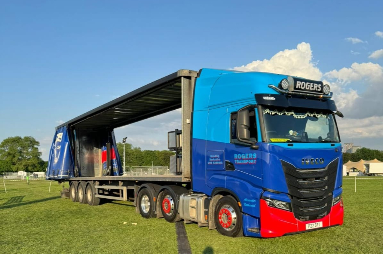 Blue and red Rogers Transport IVECO with flat trailer at an event site